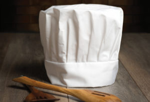 Chef's hat with wooden spoons on abstract wall background